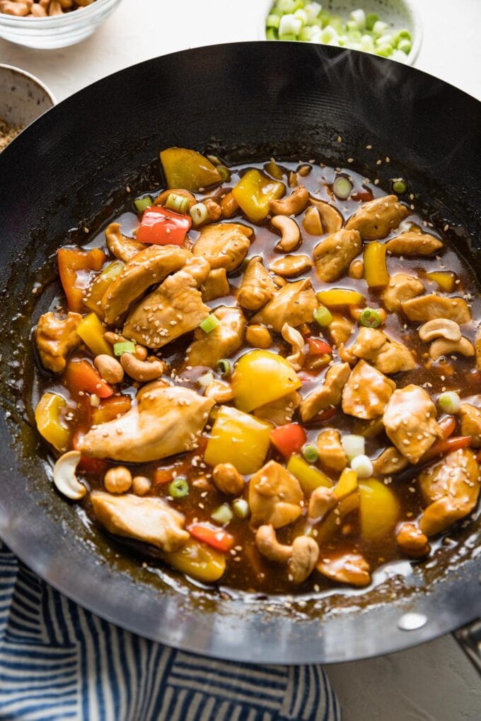 Wok filled with a chicken and bell pepper stir fry with cashews and a garnish of sesame seeds.