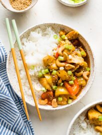 Bowl filled with rice and a stir fry with chicken, bell peppers, and cashews.