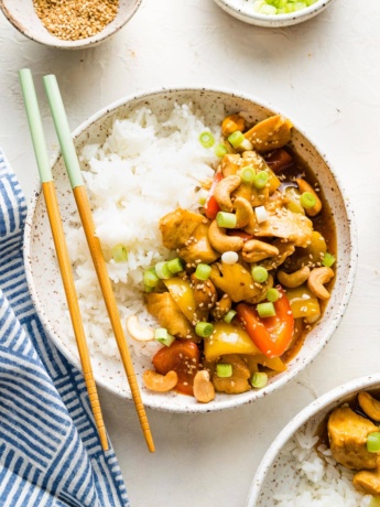Bowl filled with rice and a stir fry with chicken, bell peppers, and cashews.