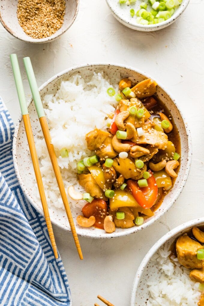 Bowl filled with rice and a stir fry with chicken, bell peppers, and cashews.