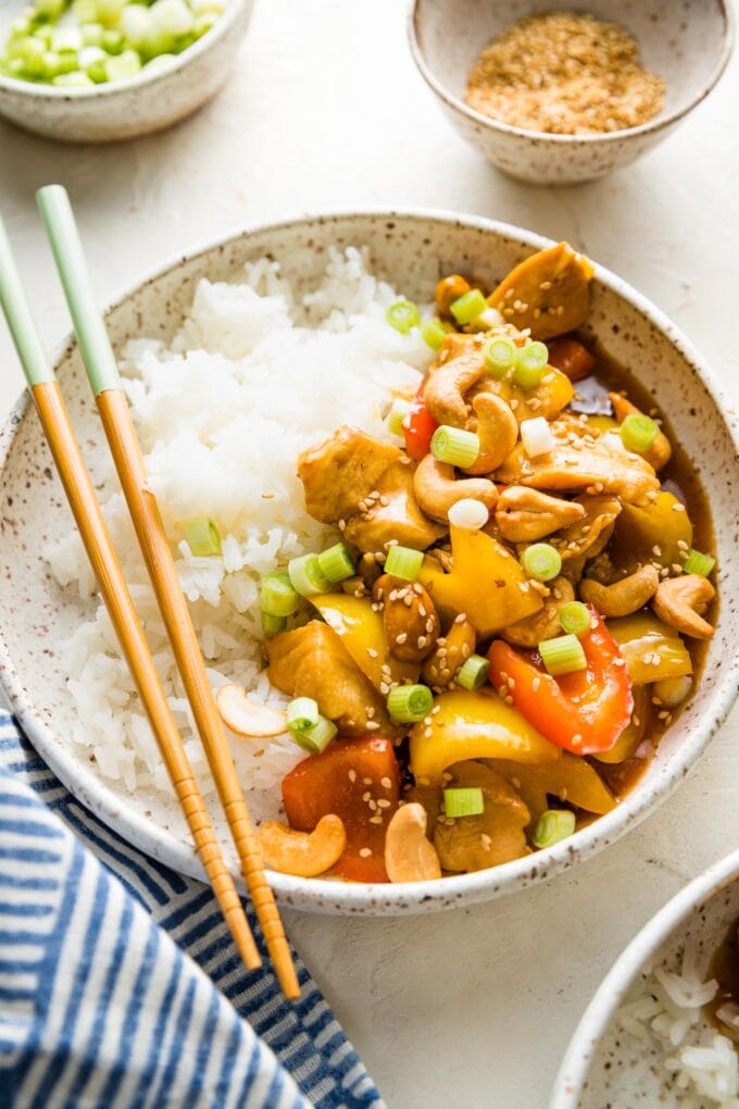 Close up of a chicken and bell pepper stir fry served with rice in a bowl.