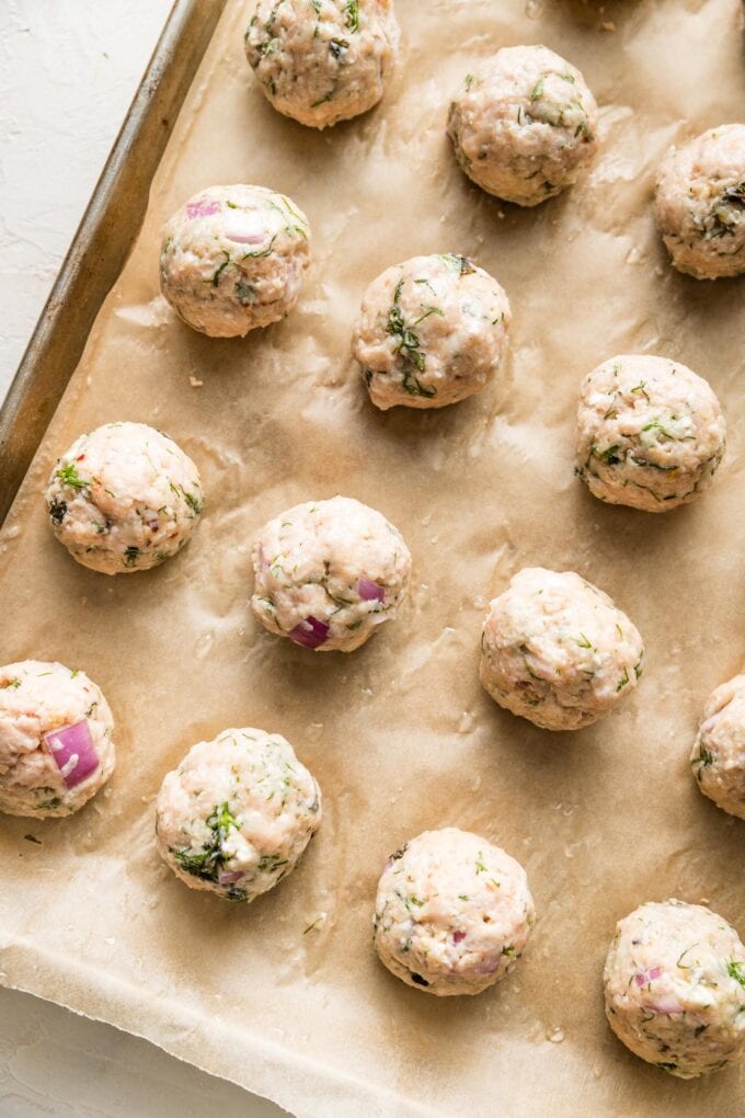 Rolled meatballs placed on a sheet pan and ready to bake.