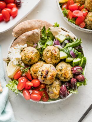 Bowl of Greek chicken meatballs served with lettuce and veggies.