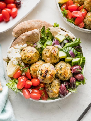 Bowl of Greek chicken meatballs served with lettuce and veggies.