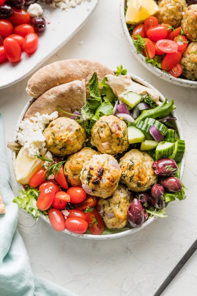 Bowl of Greek chicken meatballs served with lettuce and veggies.