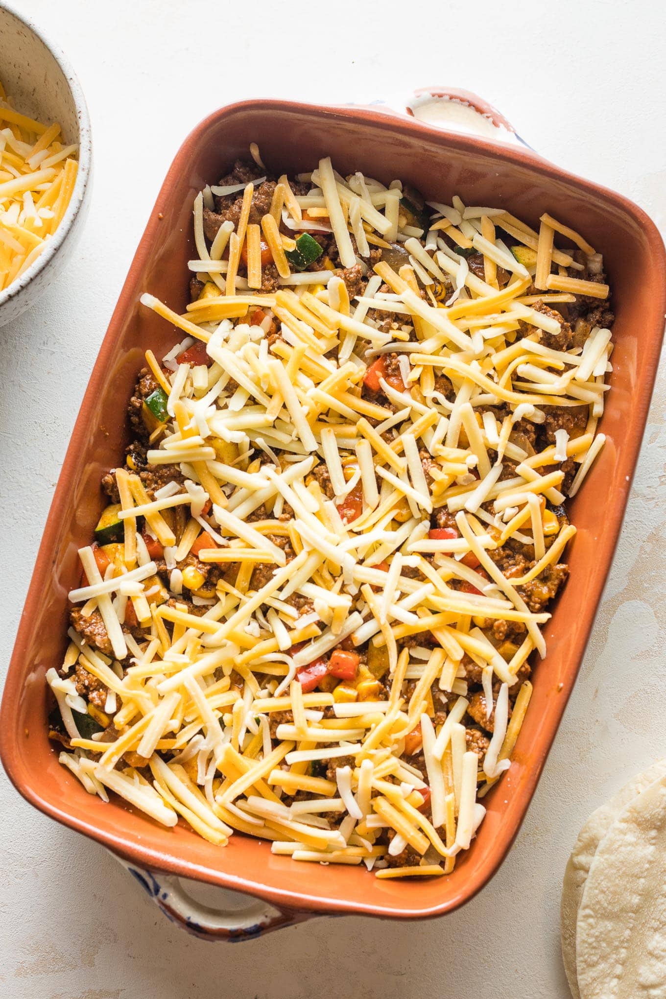 Enchilada filling and cheese layered on top of tortillas.