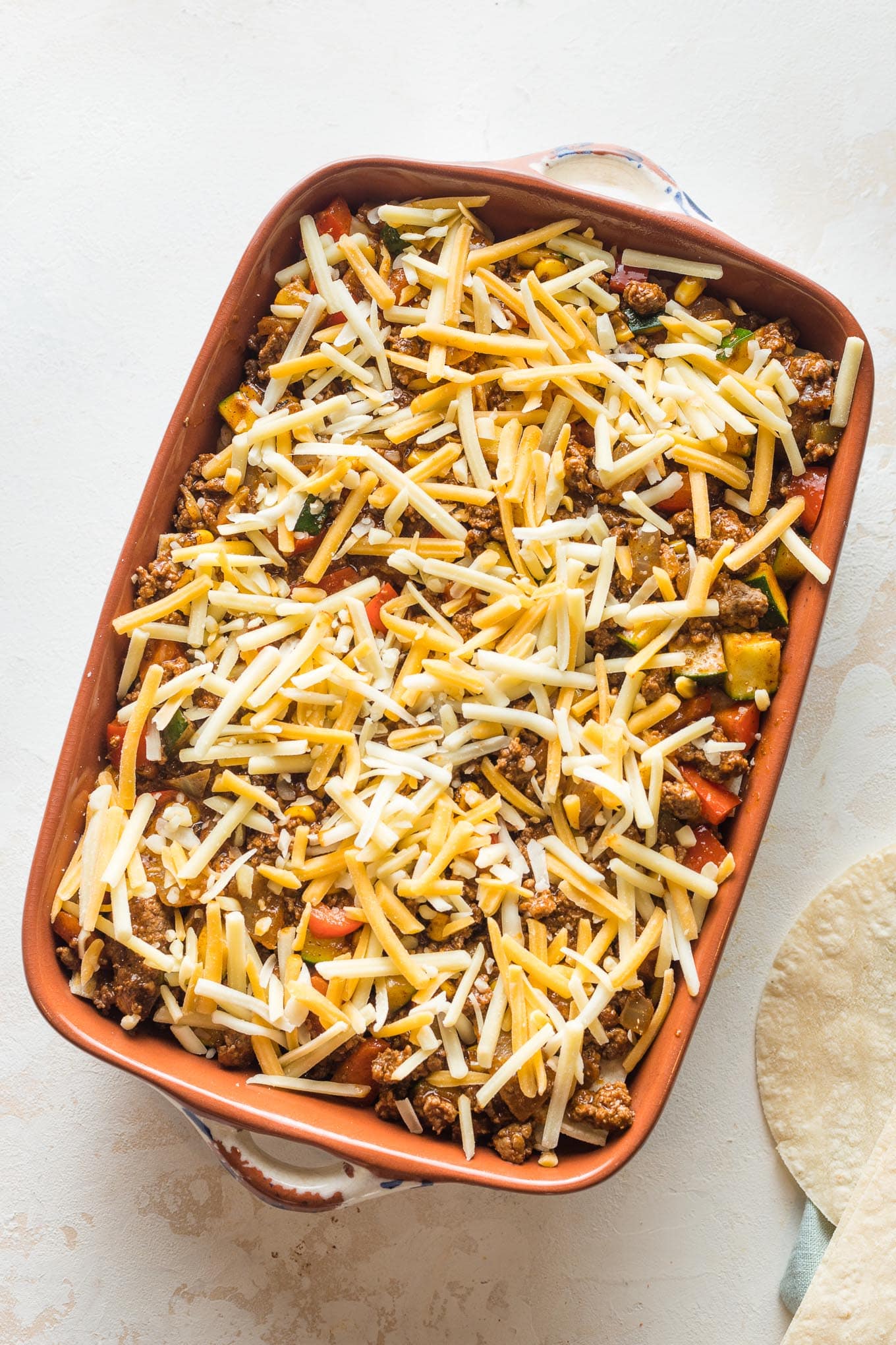 Enchilada casserole with a final sprinkle of cheese on top, ready to bake.