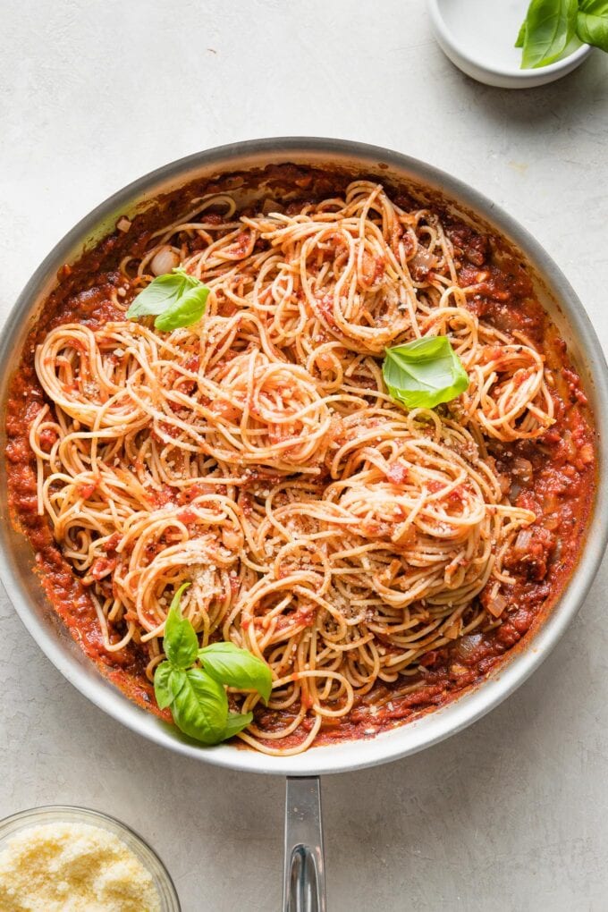 Skillet full of pasta Napoletana garnished with fresh basil leaves.