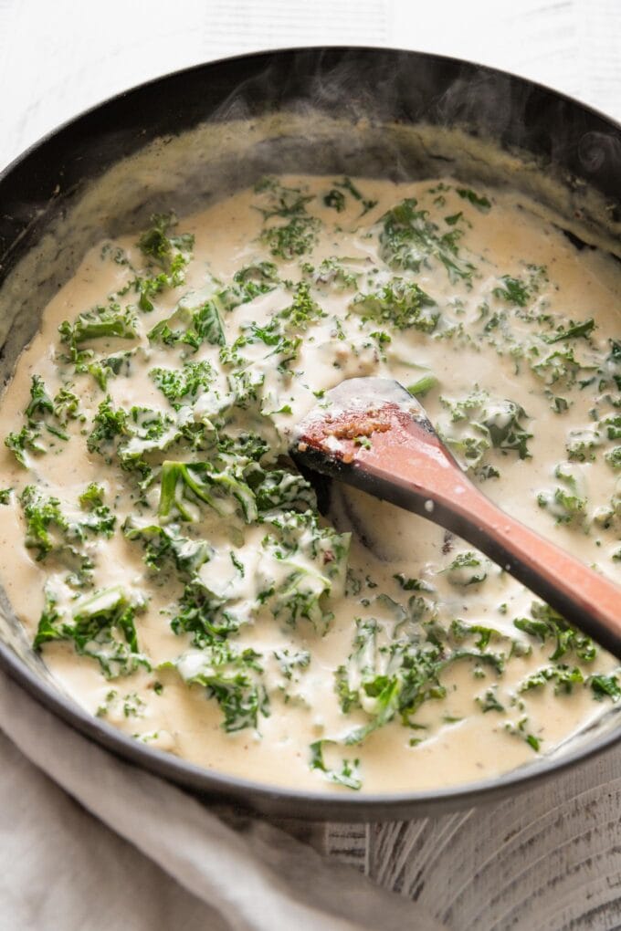 Deep cast iron skillet with an Alfredo sauce with kale mixed in.