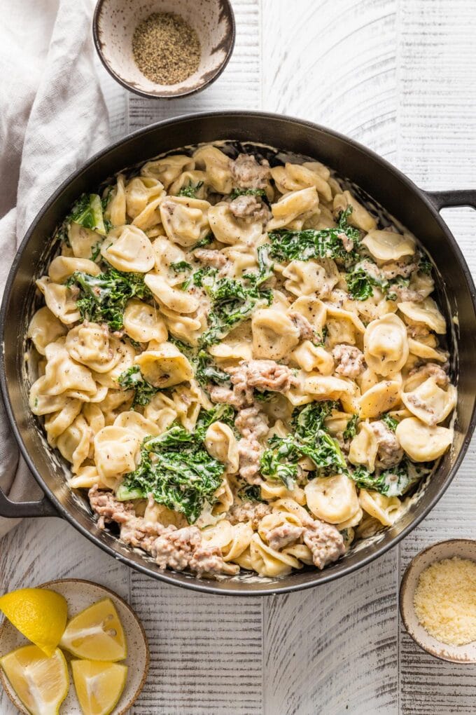 Large cast iron skillet filled with tortellini Alfredo cooked with Italian sausage and kale.