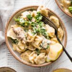 Small serving bowl with sausage tortellini Alfredo served with kale and a squeeze of lemon juice.