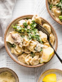 Small serving bowl with sausage tortellini Alfredo served with kale and a squeeze of lemon juice.