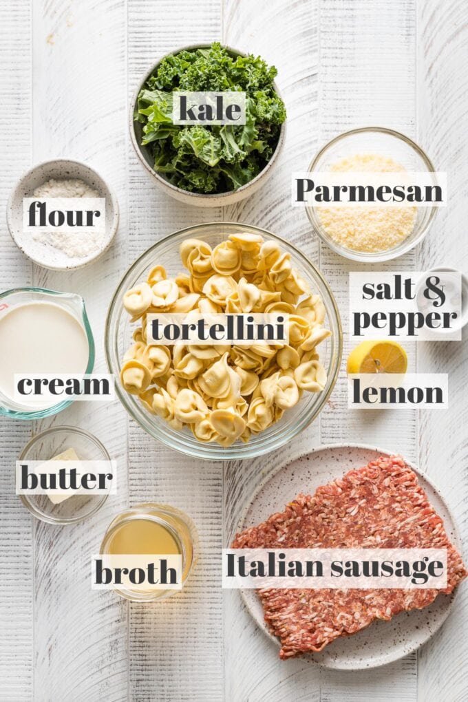 Labeled photo of prep bowls holding uncooked cheese tortellini, ground Italian sausage, kale, Parmesan, flour, cream, butter, broth, lemon, salt, and pepper.