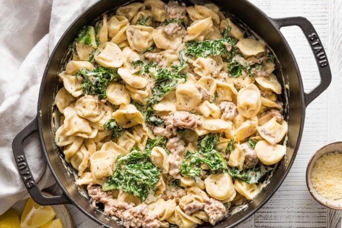 Large cast iron skillet filled with tortellini Alfredo cooked with Italian sausage and kale.