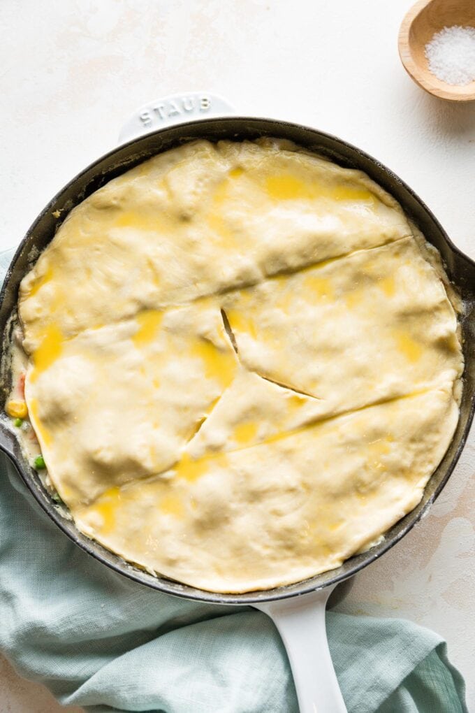 Puff pastry cut and shaped to fit on top of a skillet pot pie, brushed with egg wash and with three air vents cut in.