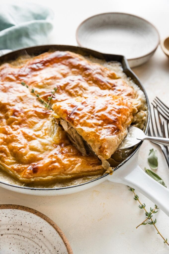 Serving spatula lifting one piece of turkey pot pie out from a cast iron skillet.