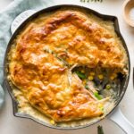 Turkey pot pie with a puff pastry crust served in a cast iron enameled skillet with one slice out.