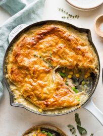 Turkey pot pie with a puff pastry crust served in a cast iron enameled skillet with one slice out.