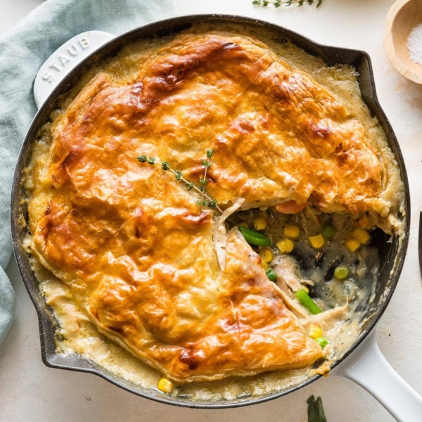 Turkey pot pie with a puff pastry crust served in a cast iron enameled skillet with one slice out.
