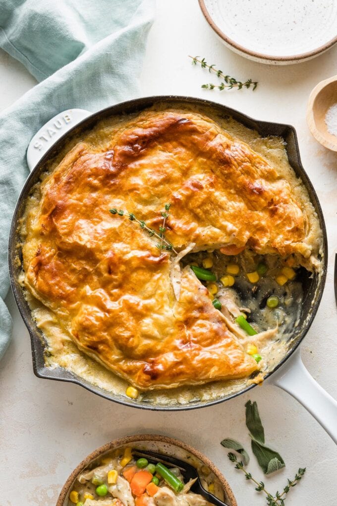 Turkey pot pie with a puff pastry crust served in a cast iron enameled skillet with one slice out.