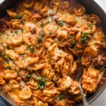 Large cast iron skillet full of baked tortellini with a spoon poised to serve.