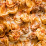 Extreme close-up of tortellini baked in a tomato meat sauce.