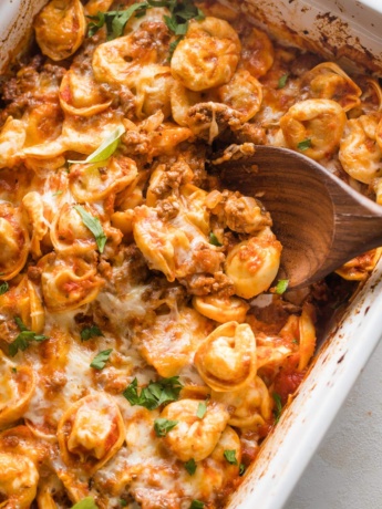 Close-up of a serving spoon scooping out a helping of cheesy baked tortellini.