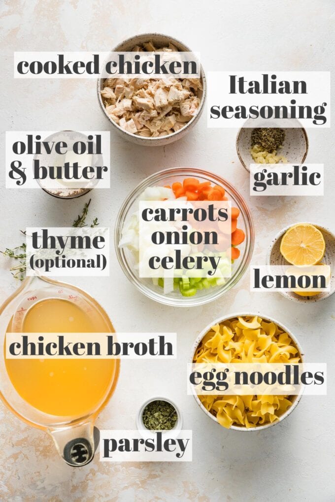 Labeled photo showing shredded rotisserie chicken, egg noodles, Italian seasoning, garlic, olive oil, butter, carrots, celery, onion, lemon, thyme, chicken broth, and parsley in prep bowls.