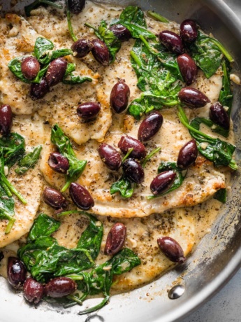 Skillet with chicken breasts in a cream sauce with Kalamata olives and wilted baby spinach.