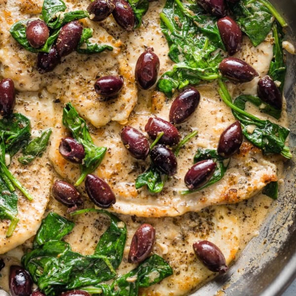 Skillet with chicken breasts in a cream sauce with Kalamata olives and wilted baby spinach.