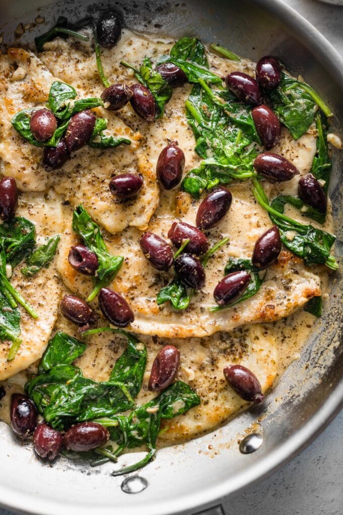 Skillet with chicken breasts in a cream sauce with Kalamata olives and wilted baby spinach.