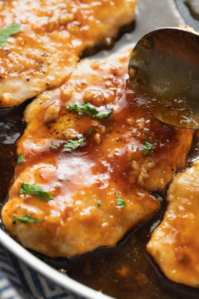 Close-up of a spoon drizzling sauce over a chicken breast.