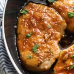 Close up of a chicken breast in a skillet covered with a honey garlic glaze.