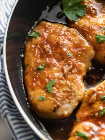 Close up of a chicken breast in a skillet covered with a honey garlic glaze.