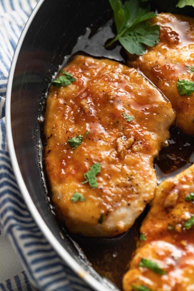 Close up of a chicken breast in a skillet covered with a honey garlic glaze.