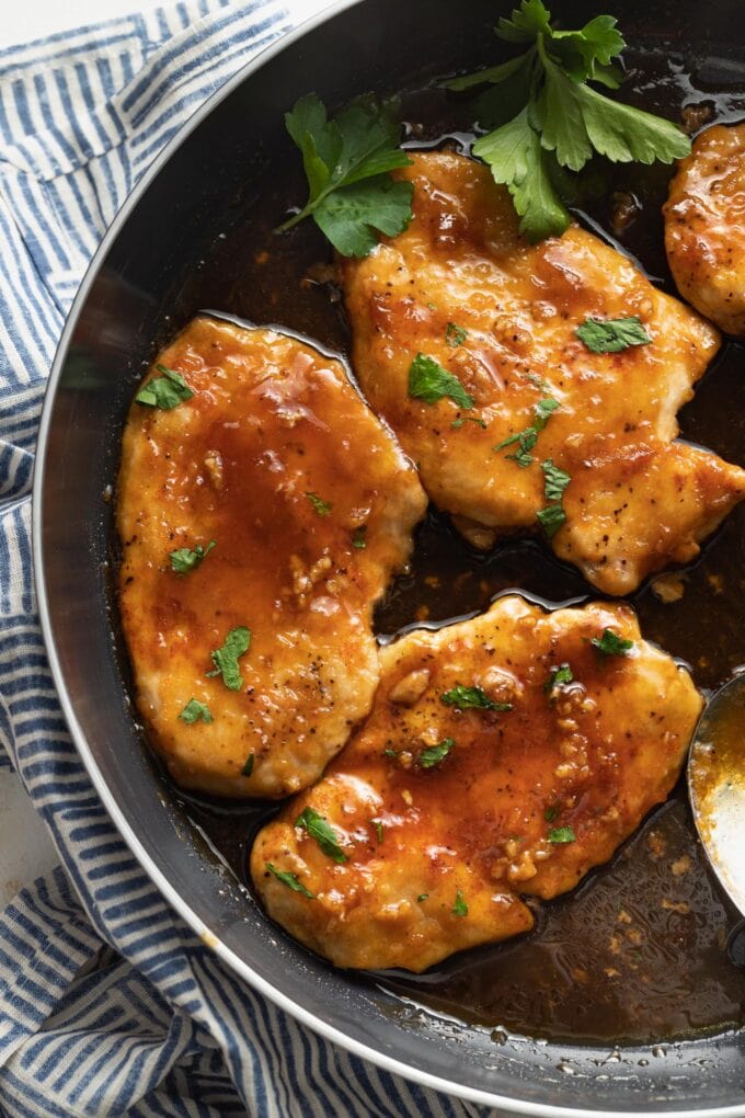 Black skillet filled with a glazed honey garlic chicken garnished with fresh parsley.