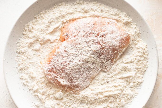 Landscape-oriented photo of a chicken breast lightly dredged through all-purpose flour.
