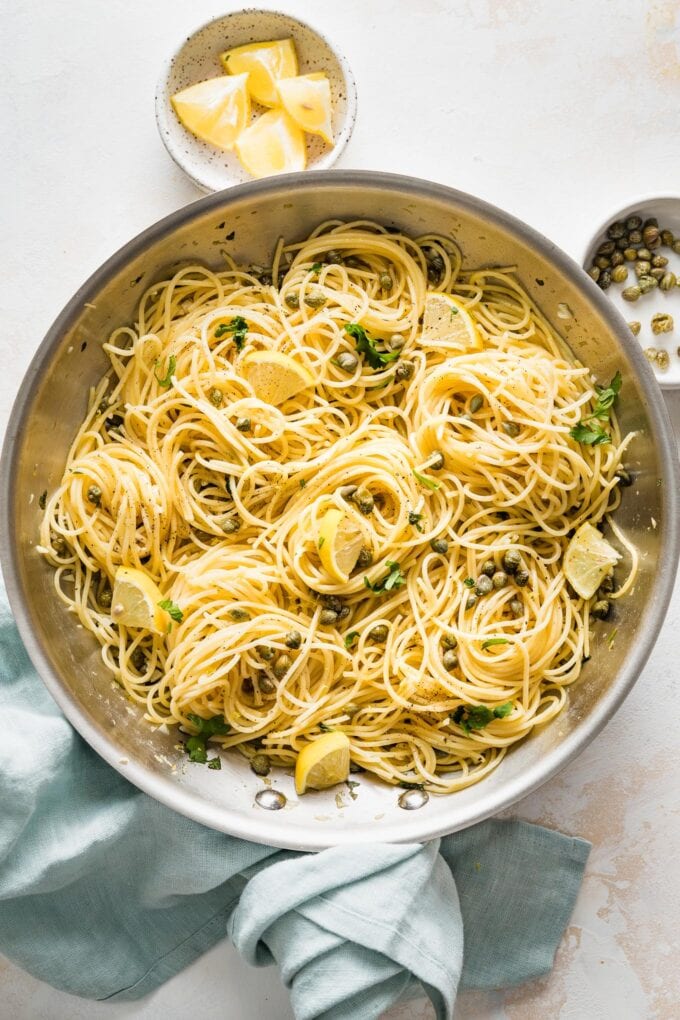 Skillet full of lemon caper pasta garnished with extra lemon wedges and parsley.
