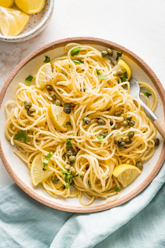 A bowl of lemon caper pasta served with extra lemon wedges and parsley.