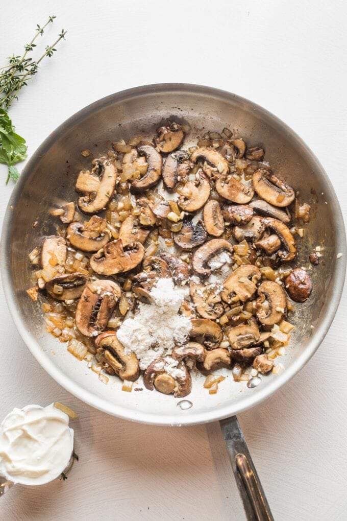 Flour sprinkled on top of cooked mushrooms in a skillet.