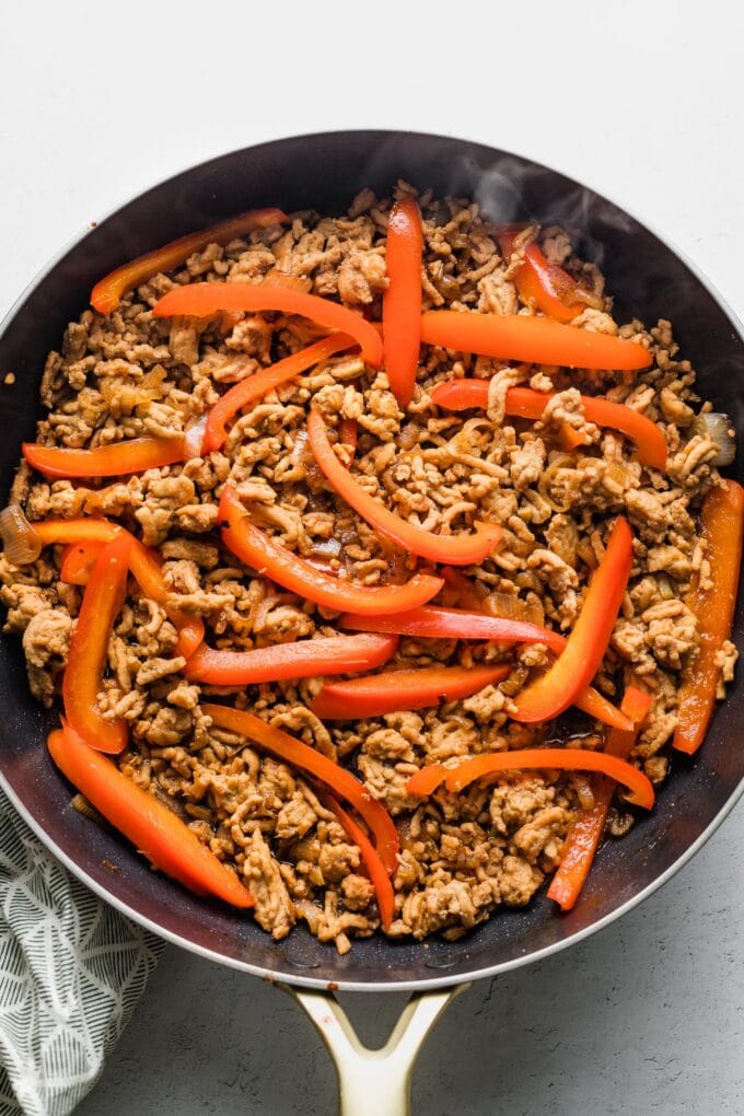 Browned chicken with sauce ingredients and sliced red bell pepper mixed in.