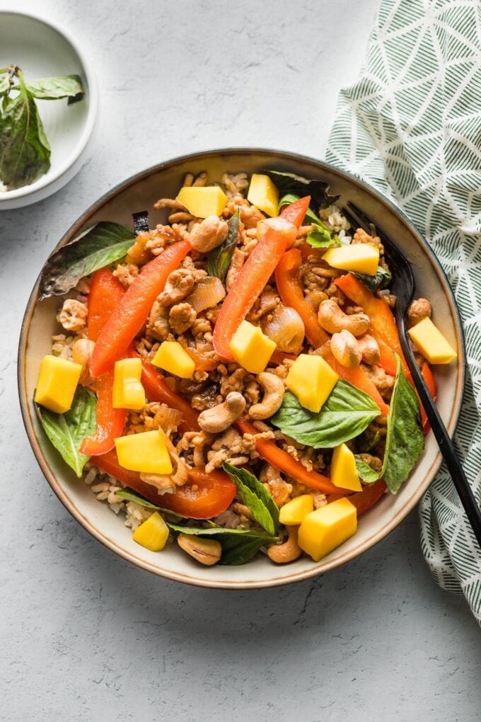 Bowl of Thai-inspired sweet basil chicken served over rice and with cashews and mango on top.