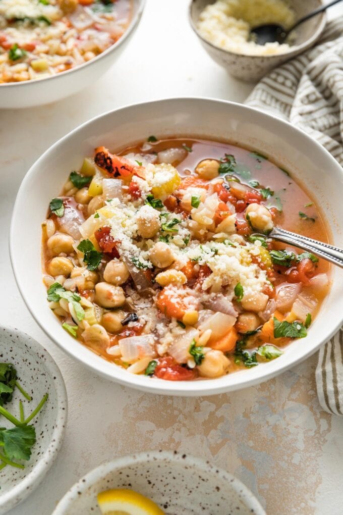 Angled view of an Italian chickpea soup being served with Parmesan and fresh parsley.