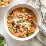 Bowl of chickpea soup with vegetables, orzo, and Mediterranean seasonings, garnished with parsley and Parmesan.