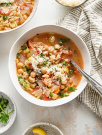 Bowl of chickpea soup with vegetables, orzo, and Mediterranean seasonings, garnished with parsley and Parmesan.