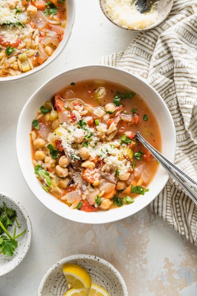 Bowl of chickpea soup with vegetables, orzo, and Mediterranean seasonings, garnished with parsley and Parmesan.