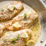 Close up of creamy lemon chicken garnished with lemon slices and fresh dill in a skillet.