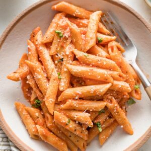 Bowl of creamy tomato pasta sprinkled with fresh grated Parmesan.