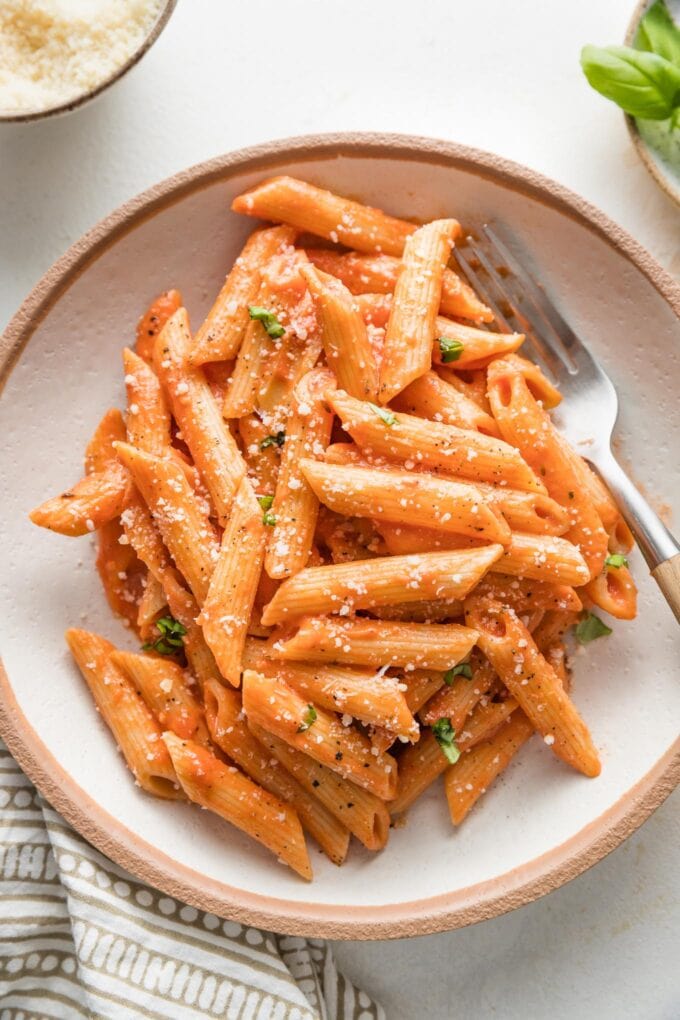 Bowl of creamy tomato pasta sprinkled with fresh grated Parmesan.