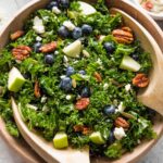 Wooden bowl holding a massaged kale blueberry salad with feta, pecans, pumpkin seeds, apple, and a homemade vinaigrette.